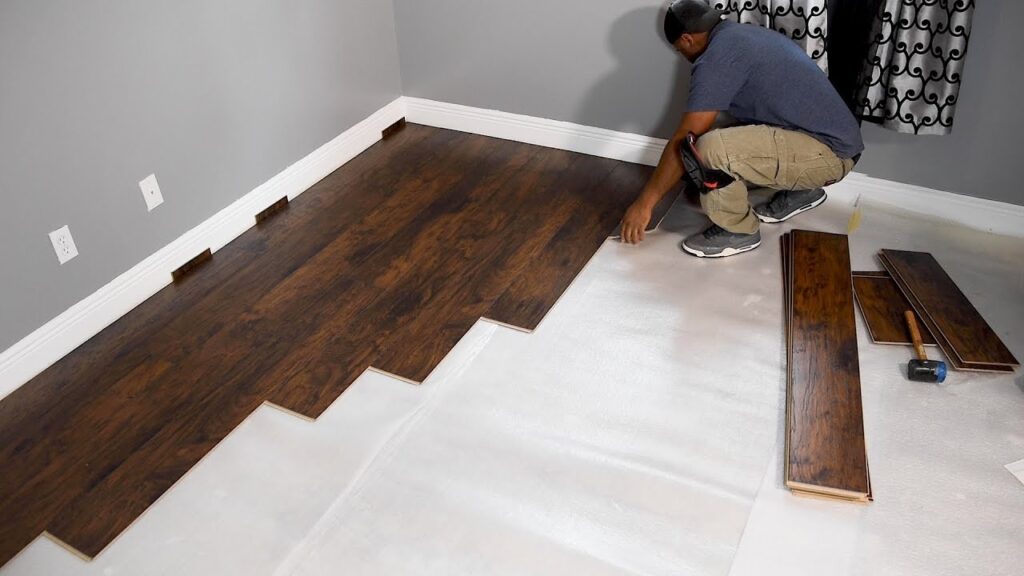Person laying down wooden floor panels in a room