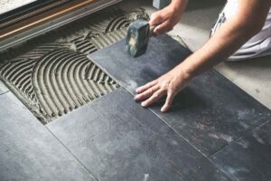 Person laying black slate tiles on a prepared surface with a trowel and hammer